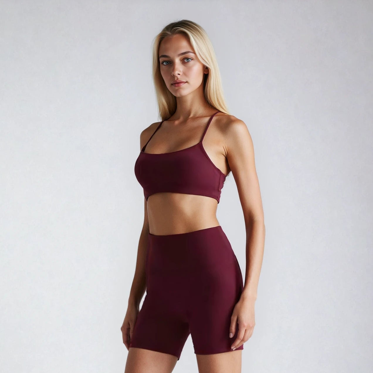 Woman wearing a burgundy sports bra and shorts set on a white background