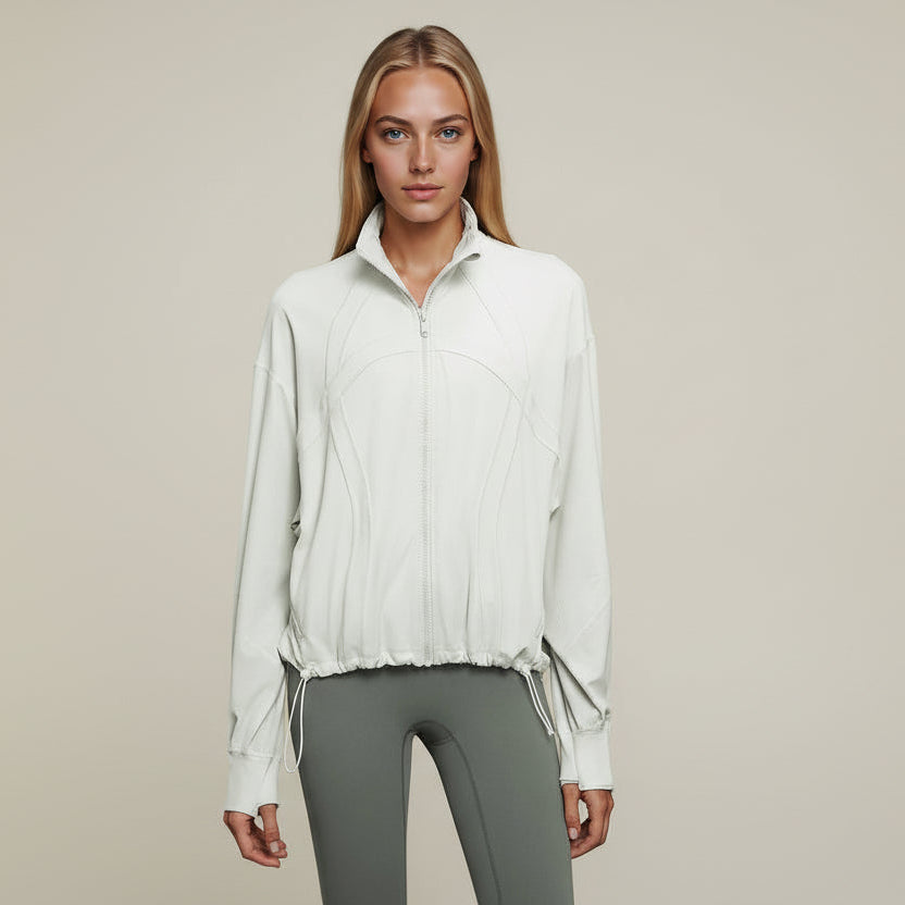 Woman wearing an Elea Active cloud white color zip-up jacket and gray pants against a dark blue background