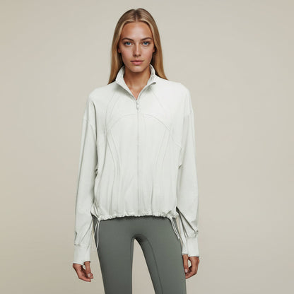 Woman wearing an Elea Active cloud white color zip-up jacket and gray pants against a dark blue background