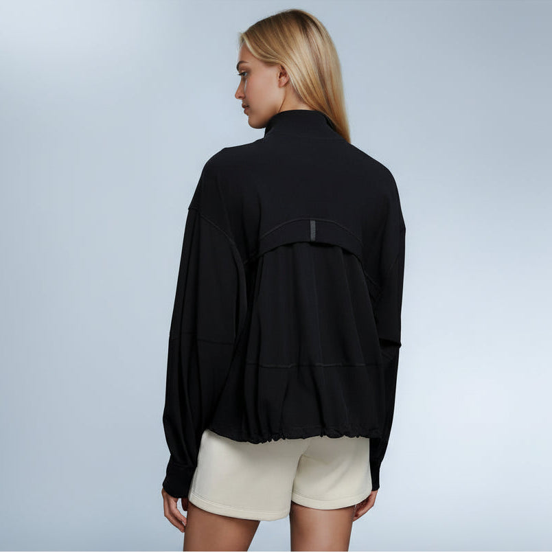 Woman wearing an Elea Active black jacket and white shorts on a gray background