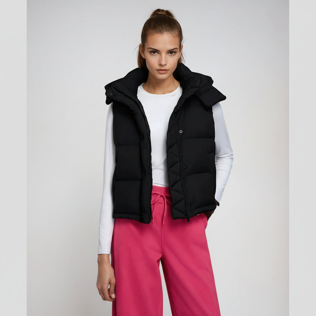 Model wearing a black puffer vest over a white shirt and pink pants on a light gray background