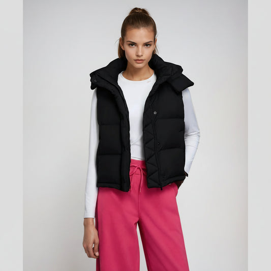 Model wearing a black puffer vest over a white shirt and pink pants on a light gray background