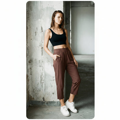 Woman wearing a black tank top and coffee brown joggers standing against a concrete wall.