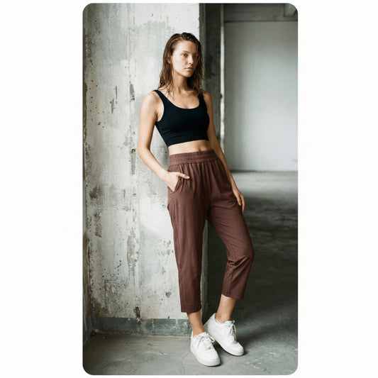 Woman wearing a black tank top and coffee brown joggers standing against a concrete wall.