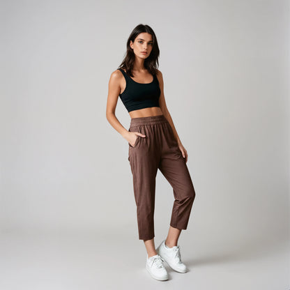 Woman wearing a black tank top and coffee brown joggers standing against a concrete wall.